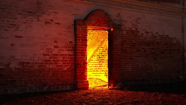 Basement door opens revealing stairs going down with red light glowing from the underground. Frightening old brick basement entrance.