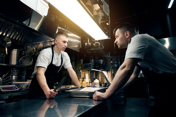Competitor chefs with knives looking at each other at table in restaurant