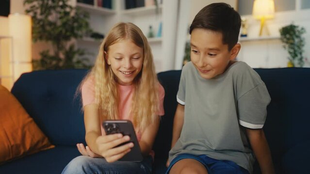 Happy young boy and girl watching funny videos on social media, using cellphone