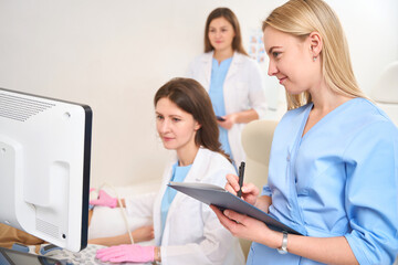 Fototapeta premium Gynecologist doing ultrasound scan of woman belly and doctor writing examining
