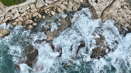 The colorful waters of the ocean swirl around the rocky and beautiful coastline. Sea waves passing over the rocks.