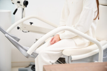 Partial of female patient sitting and waiting on medical couch in blurred clinic