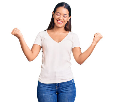 Young beautiful latin girl wearing casual white t shirt very happy and excited doing winner gesture with arms raised, smiling and screaming for success. celebration concept.