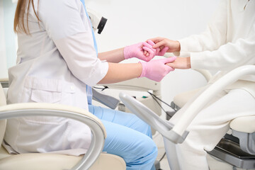 Side partial of female gynecologist and woman patient holding hands in clinic
