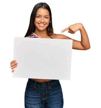 Beautiful hispanic woman holding blank empty banner pointing finger to one self smiling happy and proud
