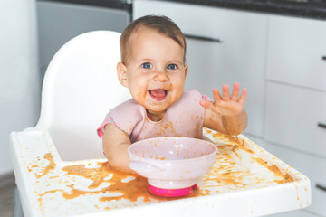 happy fun cheerful messy baby 9 months old sits in a highchair and eats lure vegetable puree soup, the concept of baby food and childhood