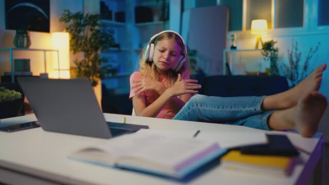Carefree young girl in headphones listening to music instead of doing homework