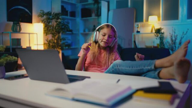 Girl in headset listening to music instead of studying, sitting barefoot at desk