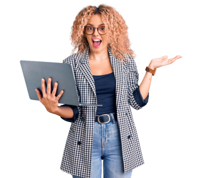 Young blonde woman with curly hair working using laptop screaming proud, celebrating victory and success very excited with raised arms
