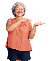 Senior woman with gray hair wearing orange tshirt amazed and smiling to the camera while presenting with hand and pointing with finger.