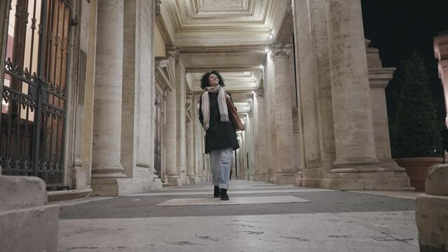 Stylish business woman walk on passage columns at Direzione museum at Capitoline in Rome, Italy at night, slow motion
