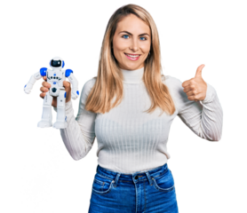 Young blonde woman holding robot toy smiling happy and positive, thumb up doing excellent and approval sign