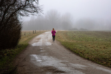 Natural landscape of a foggy morning in the countryside and an athletic woman runs along the road in sportswear.