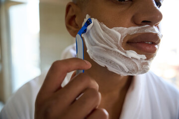 Obscure face of african american man shaving with razor in bathroom at morning