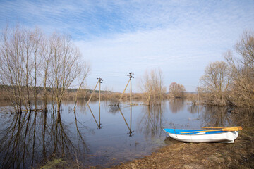 An empty boat on the shore of the overflowing floodplain of the river in spring.