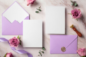 Blank white invitation cards with violet envelopes and roses buds. Wedding stationery set. Flat lay, top view, copy space.