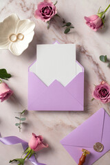 Violet envelope with blank paper card, golden rings, roses flowers on marble background. Wedding stationery set, top view.