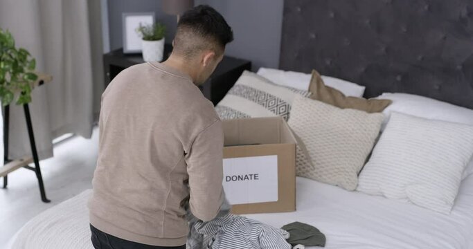 Care, man and packing of clothes for donation, back in charity organisation with kindness in bedroom. Person, humanity support or giving of clothing in box, spring cleaning or generosity in above
