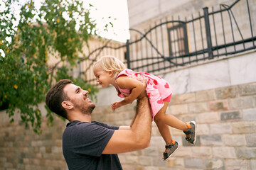 Smiling dad lifts a high laughing little girl. Portrait. High quality photo