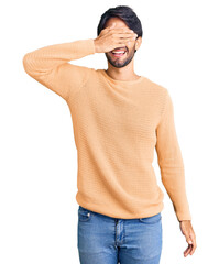 Handsome hispanic man wearing casual sweater smiling and laughing with hand on face covering eyes for surprise. blind concept.