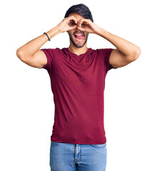 Handsome hispanic man wearing casual clothes doing ok gesture like binoculars sticking tongue out,...