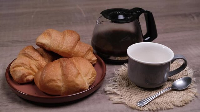 Cornetti nel piatto per la colazione con caffè nella tazza, caraffa con caffè sulla tavola