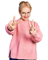 Young blonde woman wearing casual clothes and glasses smiling looking to the camera showing fingers...