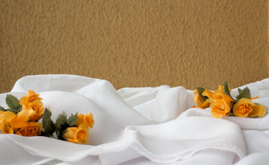 Horizontal abstract background with white fabric, orange color flowers and mustard color wall. Space for copy.