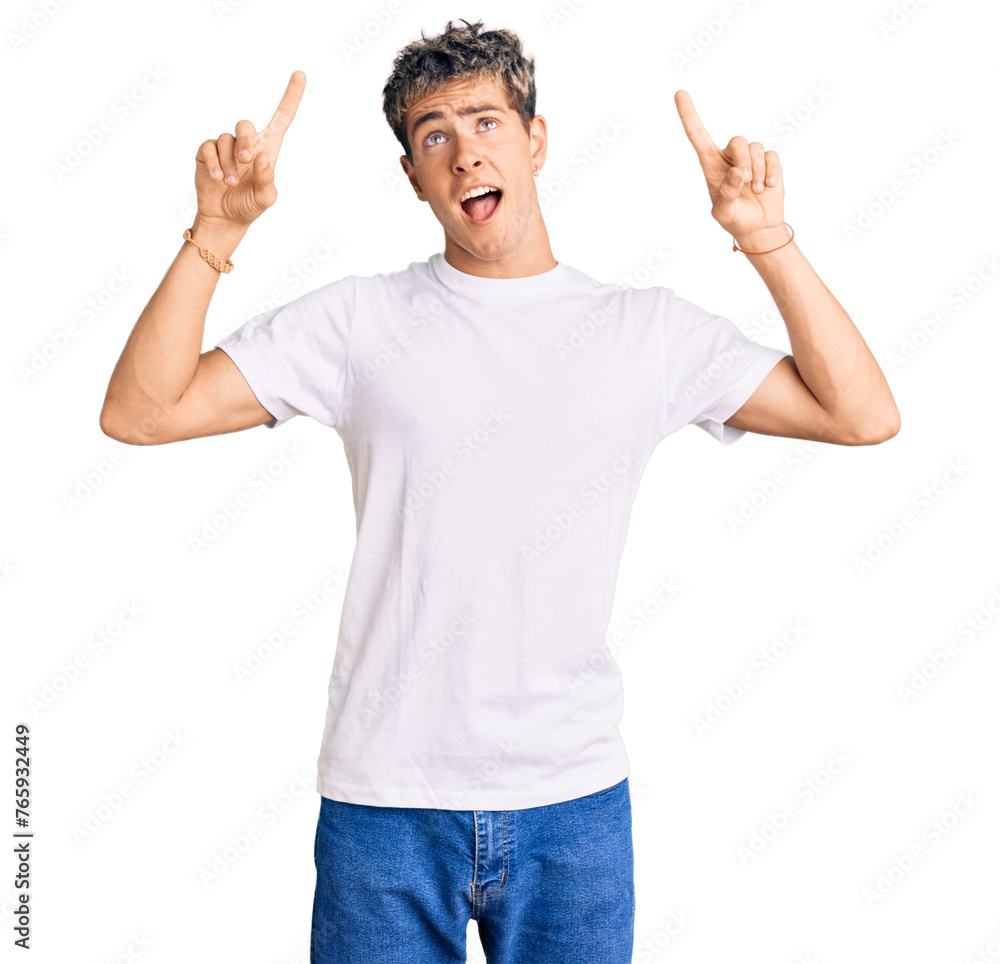 Wall mural young handsome man wearing casual white tshirt smiling amazed and surprised and pointing up with fin