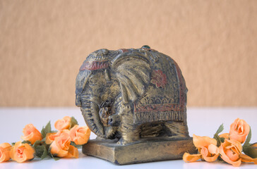 Old Indian elephant statue figure home decor on white table with orange color flowers and mustard color wall on background. Space for copy.
