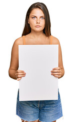 Young caucasian woman holding blank empty banner thinking attitude and sober expression looking self confident