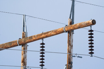 Close up view of wooden power pole with steel cables and insulators with background blue sky.