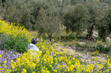 Real gray-haired woman contemplating a spring landscape of flowers and olive trees in Andalusia...