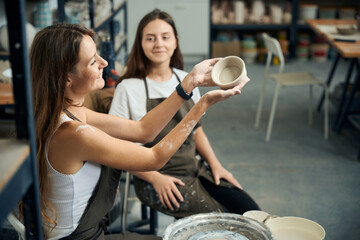 Women ceramics workers admiring beautiful clay dishes