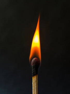 A burning match with a bright flame on a black background .
