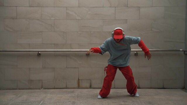 Handsome choreographer practice street dance in gray background. Young attractive b boy dancer perform while wearing stylish cloth. Feeling of lively step. Copy space. Outdoor sport 2024. Sprightly.