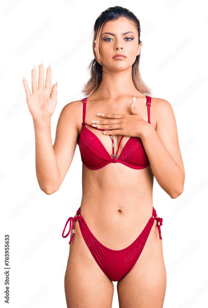 Poster young beautiful woman wearing bikini swearing with hand on chest and open palm, making a loyalty pro