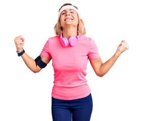 Fototapeta na wymiar Young blonde woman wearing sportswear and headphones very happy and excited doing winner gesture with arms raised, smiling and screaming for success. celebration concept.