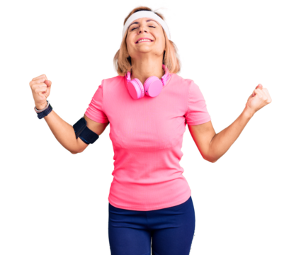 Young blonde woman wearing sportswear and headphones very happy and excited doing winner gesture with arms raised, smiling and screaming for success. celebration concept.
