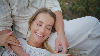 Smiling girlfriend enjoying book with man at bench closeup. Macho reading aloud