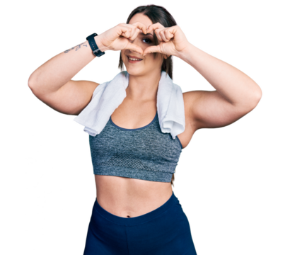 Young hispanic girl wearing sportswear and towel doing heart shape with hand and fingers smiling looking through sign