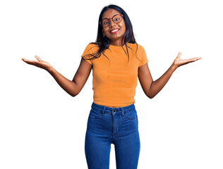 Young indian girl wearing casual clothes and glasses clueless and confused expression with arms and...