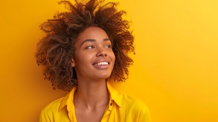 Radiant young woman with beautiful afro hair smiling against a monochrome yellow background. Portrait of a joyful young woman with stunning afro hair radiating happiness and confidence against a