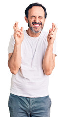 Fototapeta premium Middle age handsome man wearing casual t-shirt gesturing finger crossed smiling with hope and eyes closed. luck and superstitious concept.