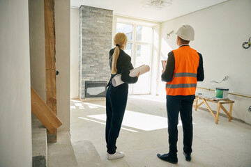 Female client and male engineer standing in room under construction