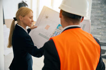 Businesswoman and engineer standing in room and looking at plan