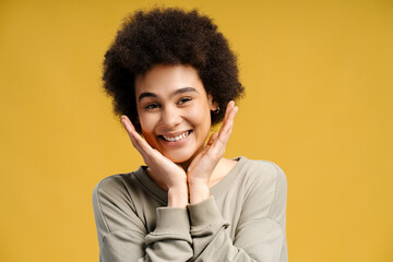 Attractive African American woman with curly hair looking at camera isolated on yellow background