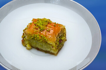 Baklava, a traditional syrupy pastry dessert. Photo of a single piece of Baklava Dessert with pistachios isolated on a white plate. View from the top diagonal.