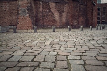Cobblestone street leading to an old brick wall, with bollards on the side, depicting vintage urban texture.