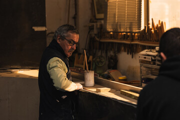 Elderly Carpenter and Latin Assistant Selecting Wood for Varnishing in Carpenter Workshop